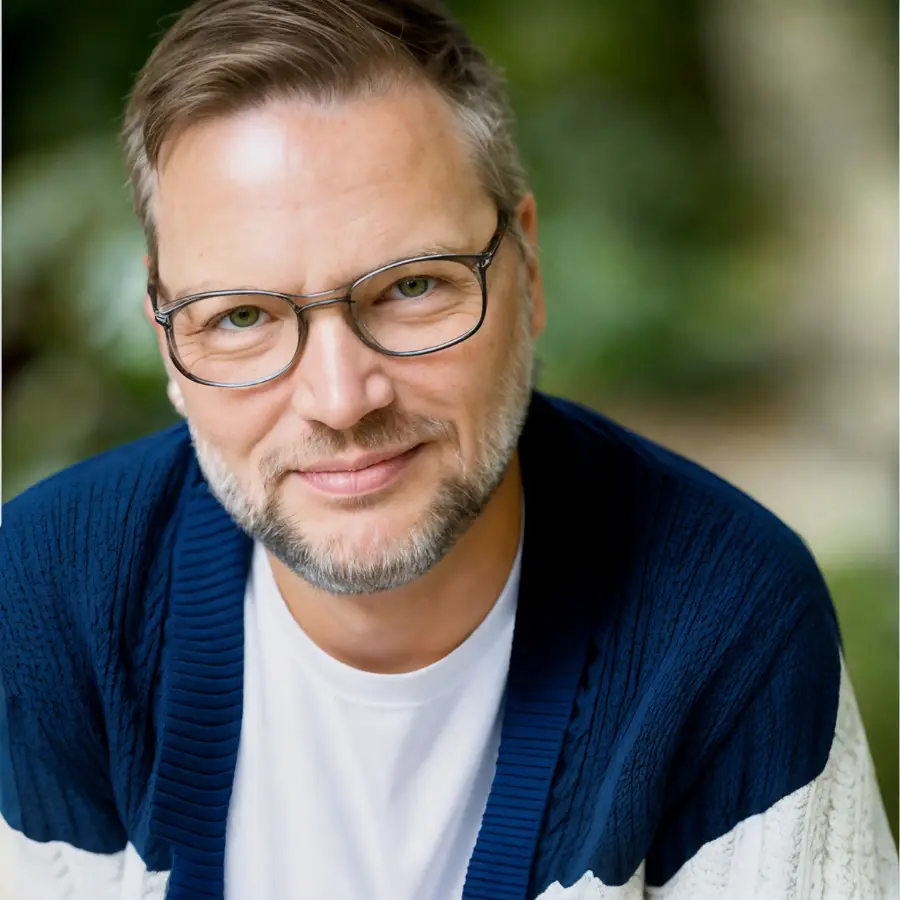Troy Johnson, LCSW, founder of Queer Talk Therapy, smiling outdoors in glasses and cardigan. LGBTQ therapy in Chicago